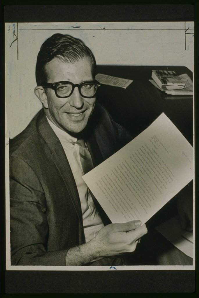 A black-and-white photograph of a smiling Albert Shanker, president of the United Federation of Teachers, seated at a desk and holding a typed report, during an earlier round of contract talks with the city.